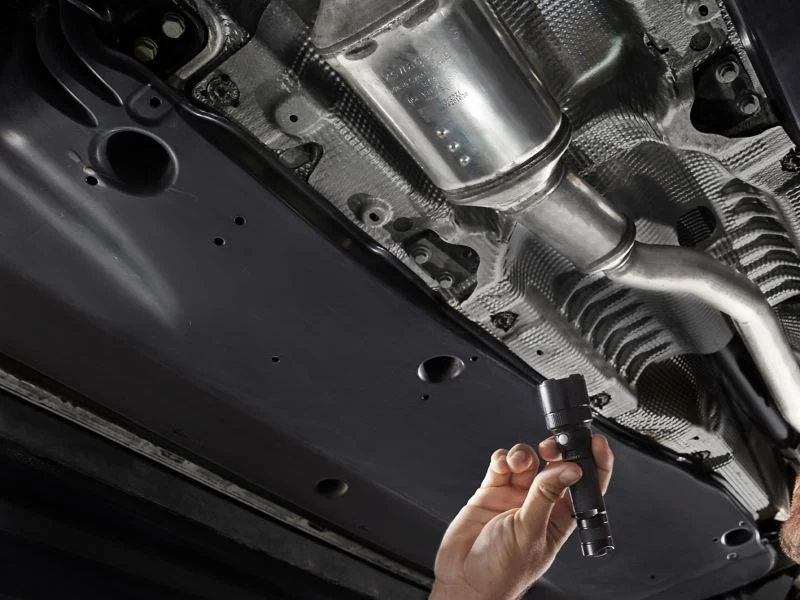 Mechanic inspecting an exhaust and emissions system from below a vehicle